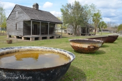 Sugar Cane kettles in front of slave shacks.