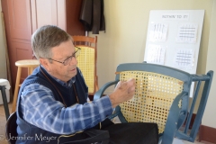 A worker demonstrates caning a chair.